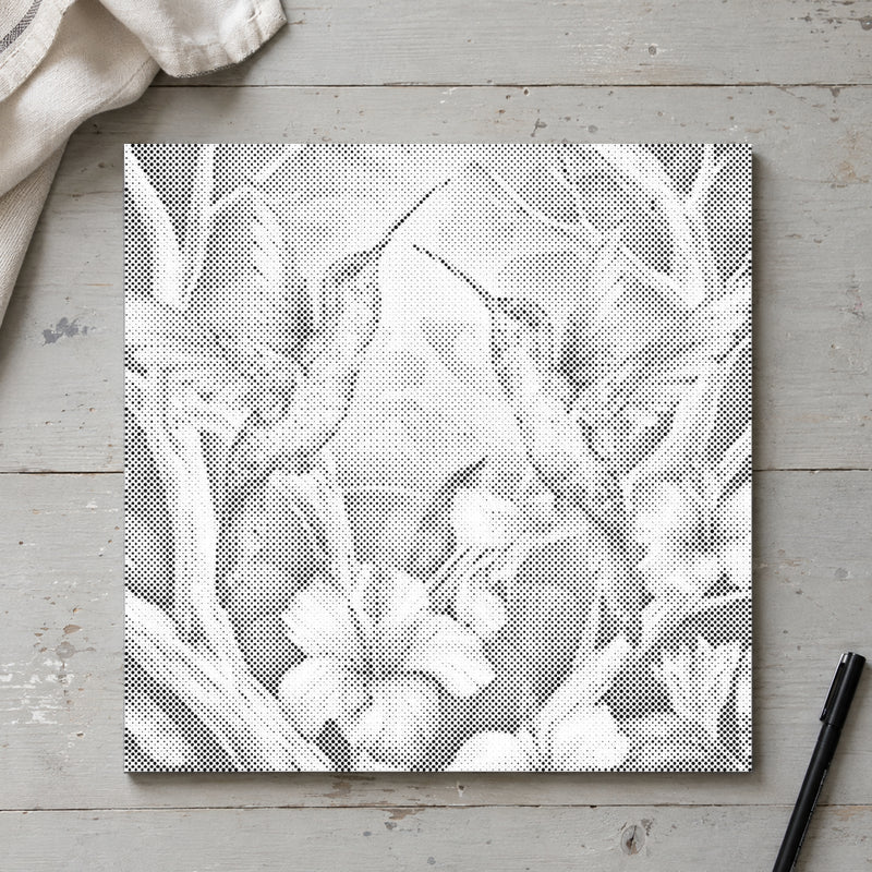 Prickmålningen “Kolibrier bland blommor”, sedd ovanifrån på ett arbetsbord i mjukt dagsljus.