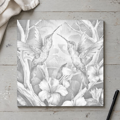 Prickmålningen “Kolibrier bland blommor”, sedd ovanifrån på ett arbetsbord i mjukt dagsljus.